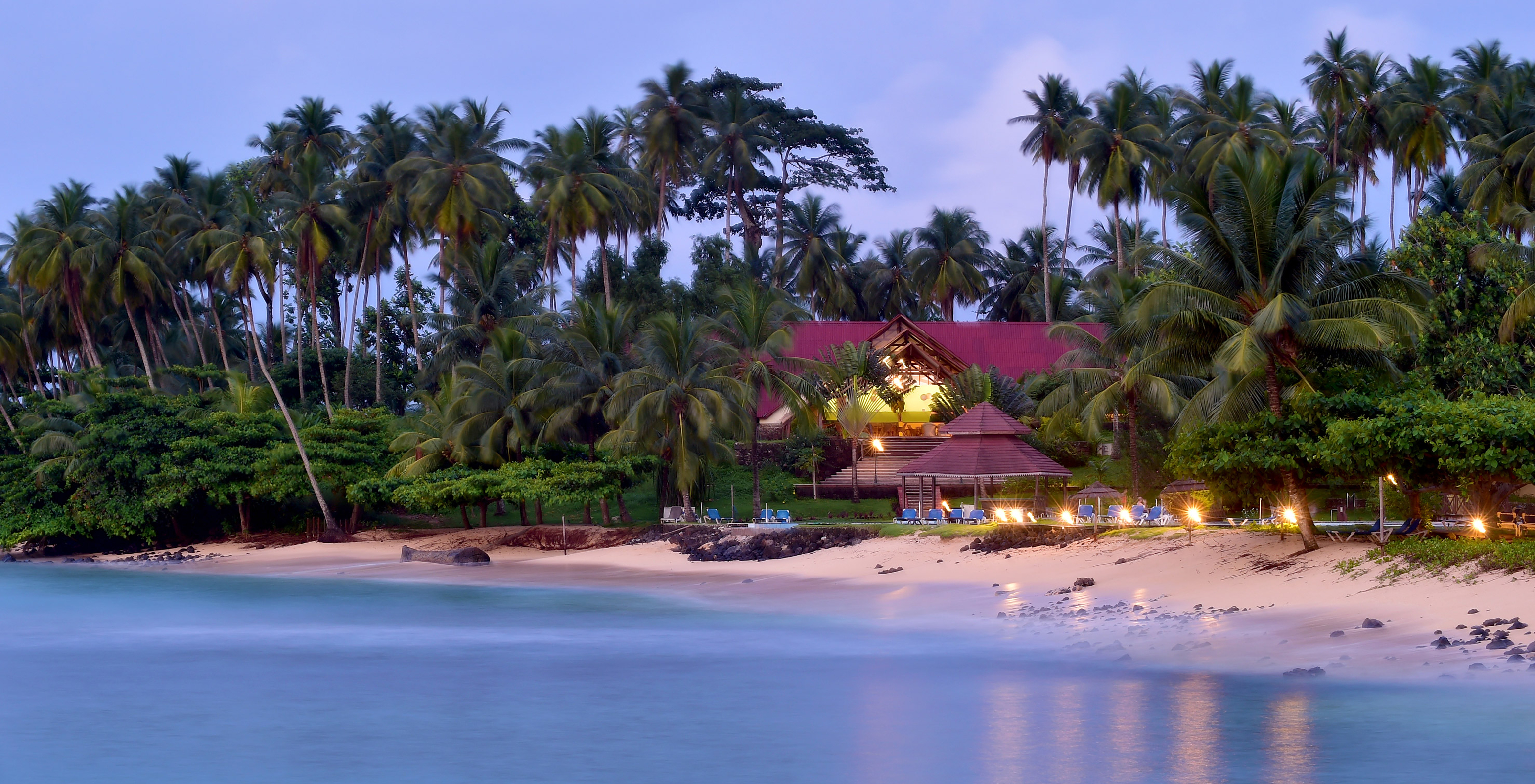 Hotel para Férias, com Piscina e Spa, em Frente à Praia ao entardecer, com palmeiras, espreguiçadeiras e focos de luzes