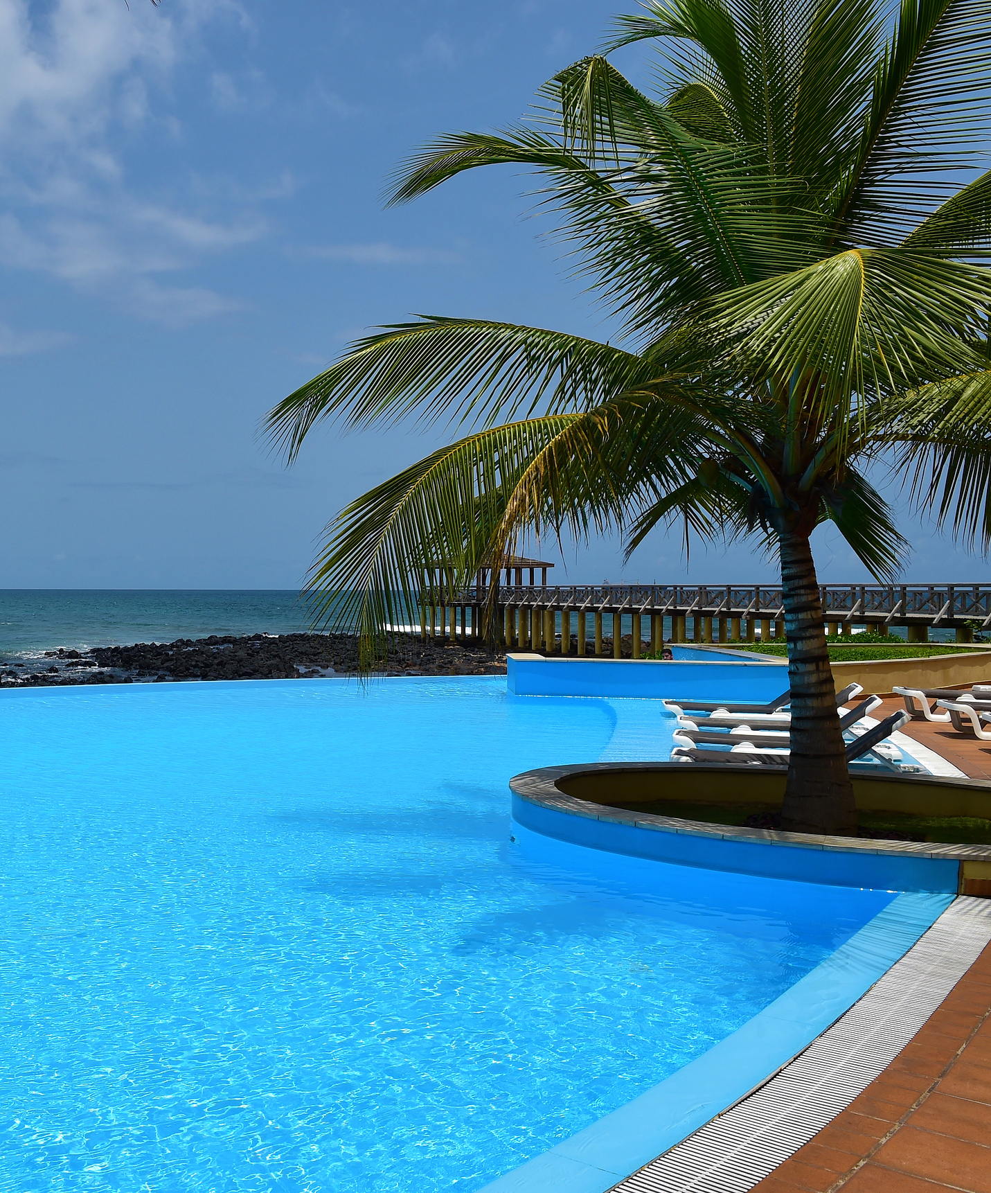 Piscina do Pestana São Tomé, com espreguiçadeiras numa paisagem magnífica com palmeiras e vista mar