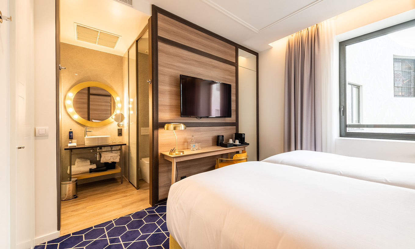 O Small Double Room do Pestana CR7 Gran Vía Madrid tem duas camas juntas e casa de banho em frente com um espelho de luzes