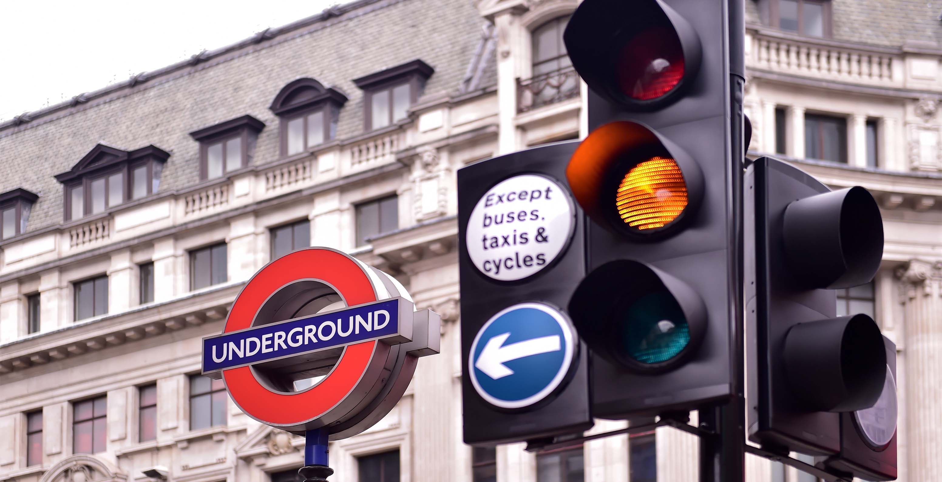 Semáforo amarelo, com sinalética do metro de Londres, com um edifício antigo atrás com várias janelas